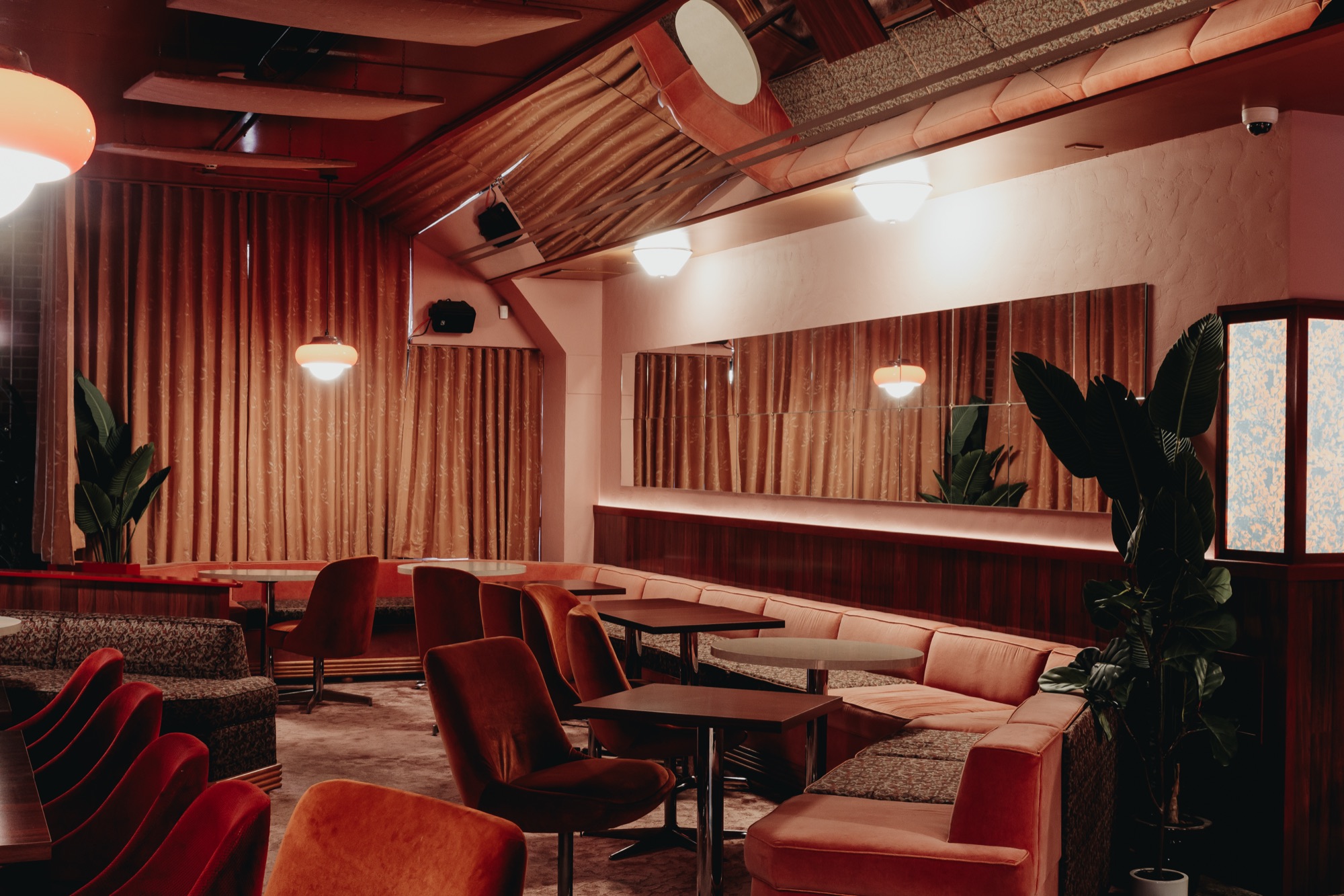 Terracotta banquette seating, velvet swivel chairs and dark cafe tables in a warmly lit restaurant lounge