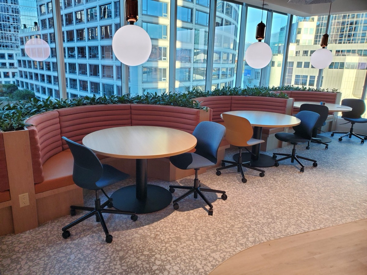 Curved salmon fluted banquette in an office lounge with round tables, task chairs and globe pendant lights
