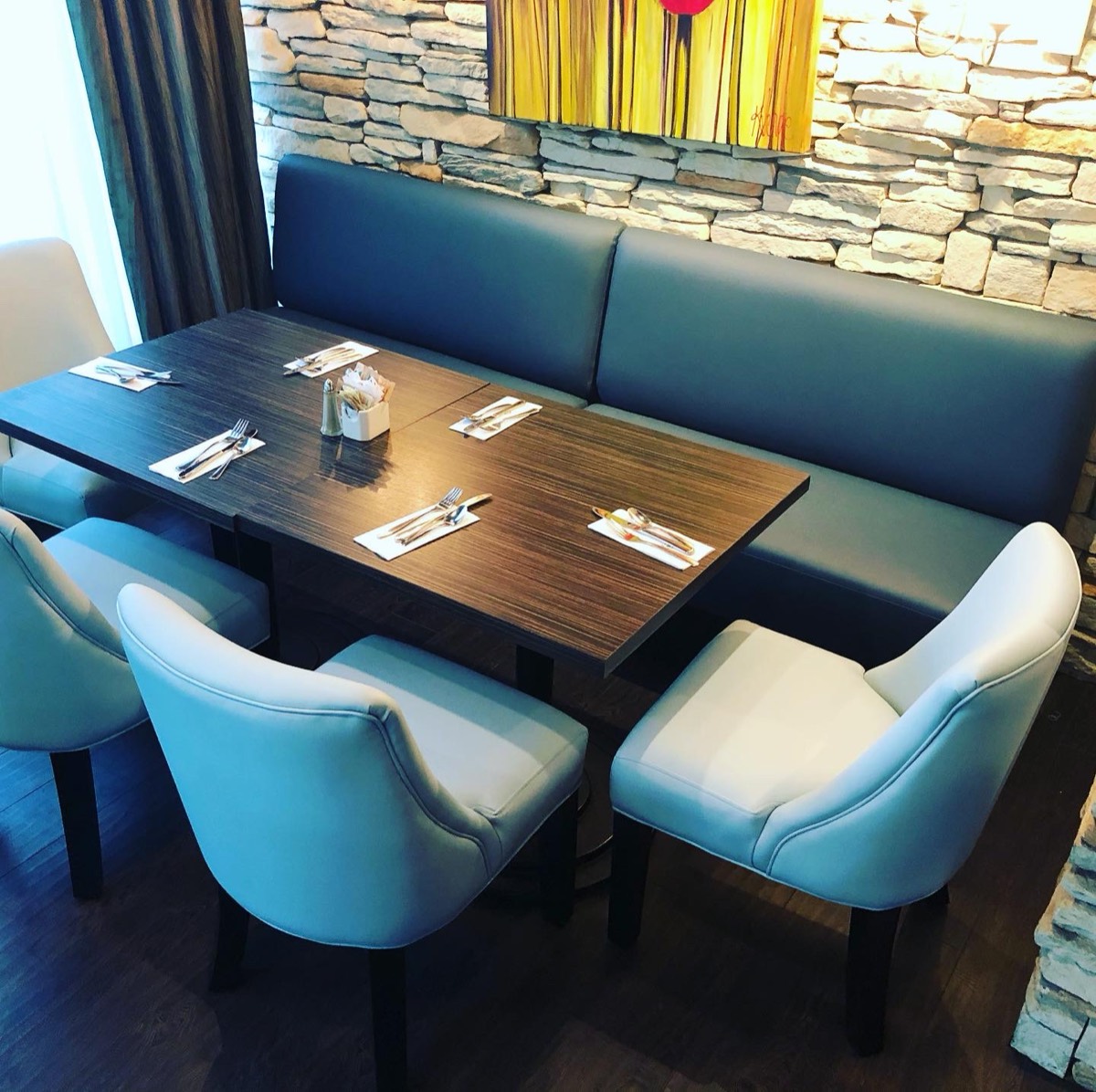 Teal booth seating with white dining chairs against a stone accent wall