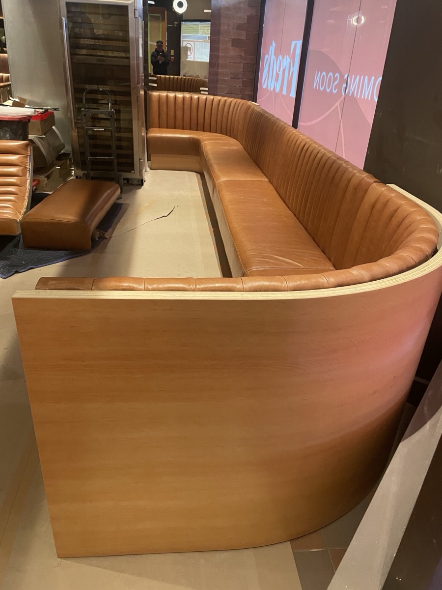 Tufted caramel leather curved booth installation behind a Coming Soon storefront sign